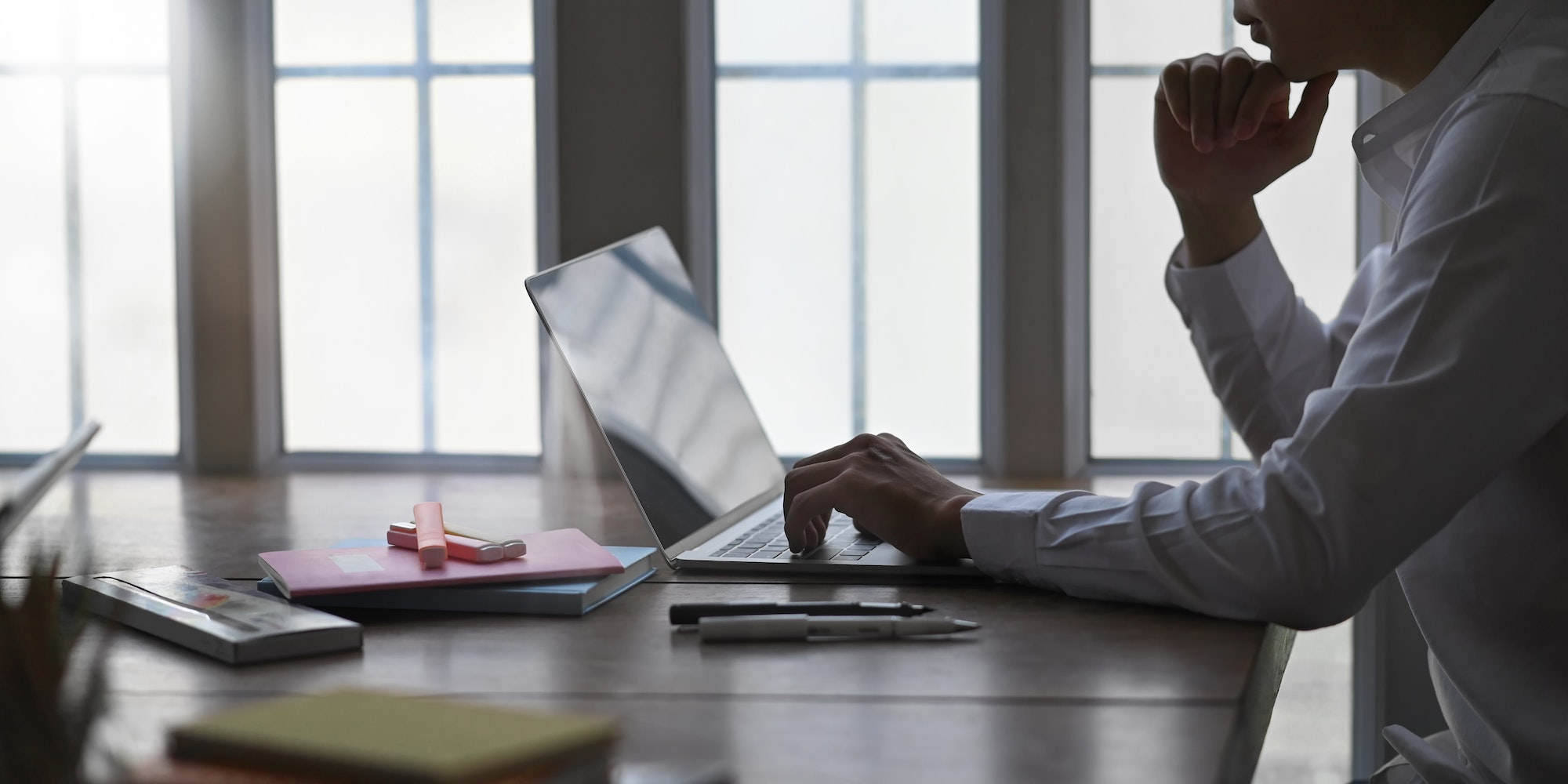 Man on white shirt keep his hand on chin while thinking and sitting in front a computer.